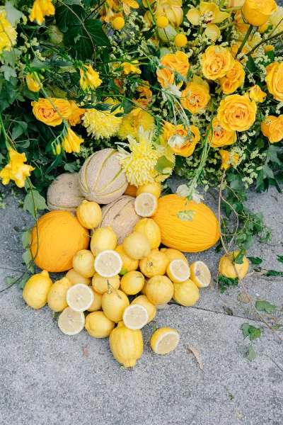 Lemon wedding decor styled as a citrus wedding arrangement with yellow roses clustered among fresh lemons, arranged low on concrete ground.