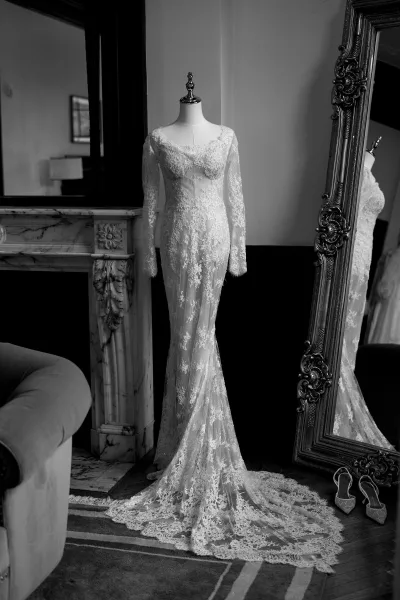 Lace wedding dress with long sleeves displayed on a mannequin near a marble fireplace, intricate lace detailing throughout