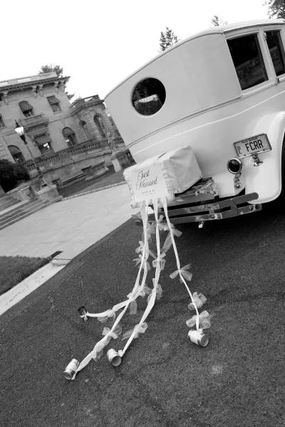 Wedding getaway car, a vintage wedding car with a Just Married sign, parked on a paved driveway by a mansion’s stone steps and lamp post.