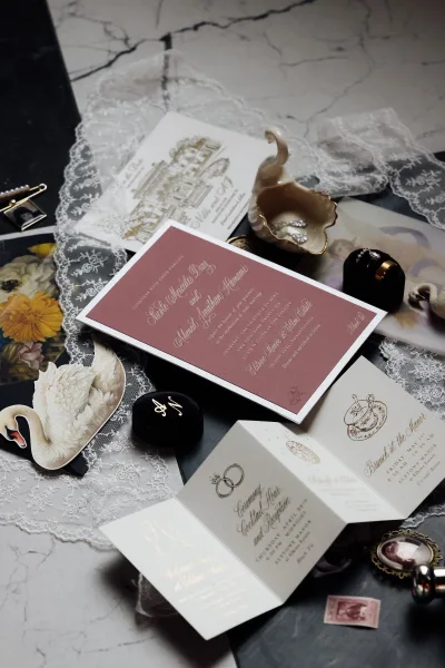 Wedding invitation suite featuring a mauve wedding invitation and gold foil stationery, styled with a velvet ring box on marble and slate.