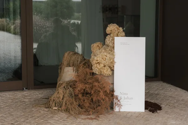 Wedding welcome sign serving as a ceremony entrance sign, styled with dried florals against glass doors with soft window reflections.