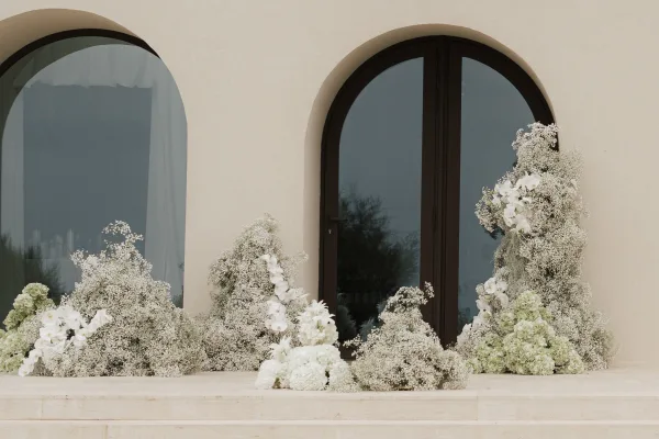 Wedding floral installation with ground floral clusters of baby's breath framing an arched doorway on a stucco wall and stone steps.