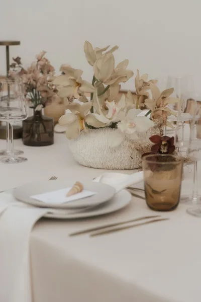 Reception tablescape with modern wedding centerpiece of orchids, arranged on ivory table linen in a soft, neutral palette.