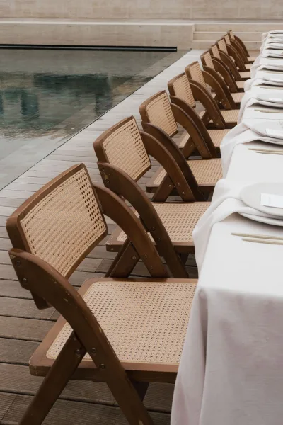 Reception table setup for a poolside wedding reception with rattan chairs arranged beside a reflecting pool on a wooden deck with stone steps.