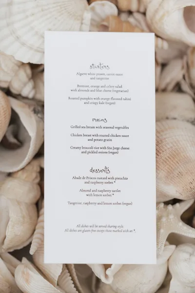 wedding menu styled as a beach wedding menu, a tall black-and-white minimalist card on white cardstock, surrounded by seashells.