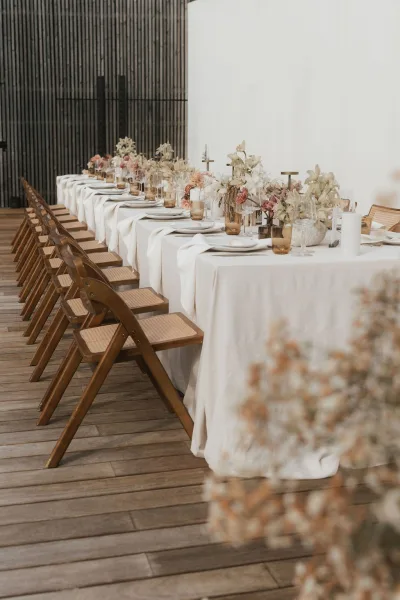 Reception tablescape spanning a long banquet table with elegant orchids, set on wood decking before a slatted wood wall backdrop.