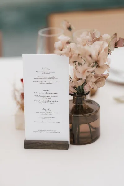 Wedding menu card with minimalist menu design, standing upright beside an amber glass vase on the table.