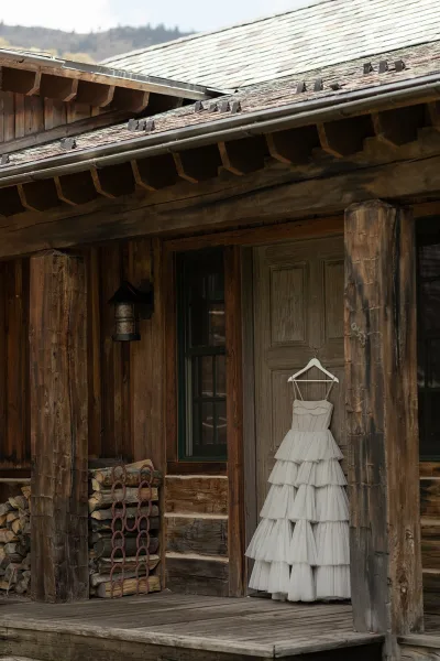Wedding dress on hanger, a white tulle bridal gown hanging from a rustic cabin door with a lantern sconce and mountain backdrop