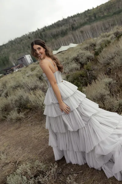 Bridal portrait of a bride looking back in a layered tulle dress on a mountain hillside path, pearl earrings visible under overcast sky