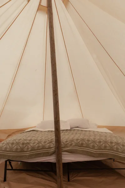 Glamping tent interior with a neatly made bed, soft pillows and duvet, centered on the tent pole beneath the canvas canopy