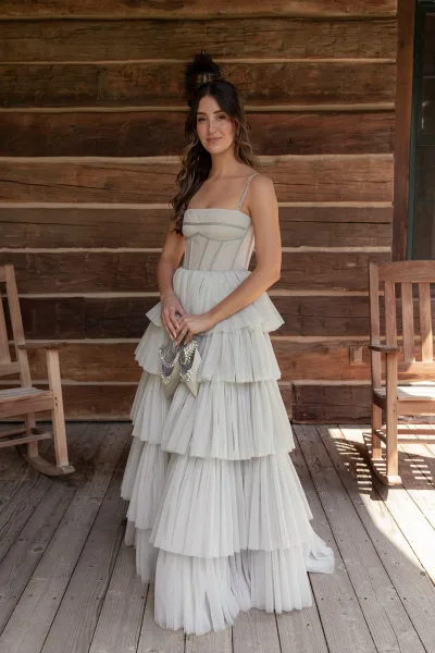 Bridal portrait of a bride holding wedding shoes, showing corset bodice and tiered tulle skirt on a wooden cabin porch with rocking chairs