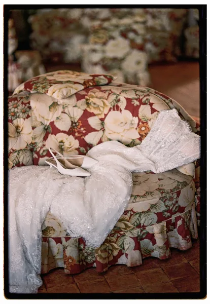 Wedding dress with lace wedding dress long sleeves draped over a floral upholstered chair, bridal shoes on a tiled floor nearby