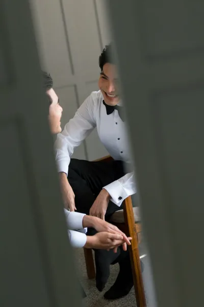 Getting ready moment during men's wedding prep as a man fastens a black bow tie with careful hands before the ceremony.