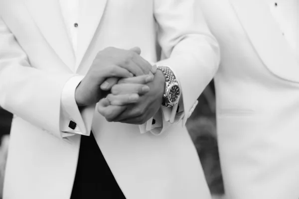 Couple holding hands in a close-up portrait, tuxedo sleeves frame their grip, accented by silver cufflinks.