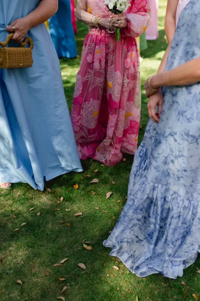 Wedding guest dresses styled for an outdoor wedding guest outfit, with floral bouquet, wicker handbag and bangles on a leafy garden lawn