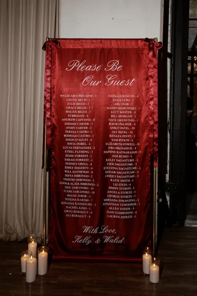 Wedding seating chart seating chart sign in calligraphy on a gold frame stand, paired with pillar candles and glass votives on wood floor