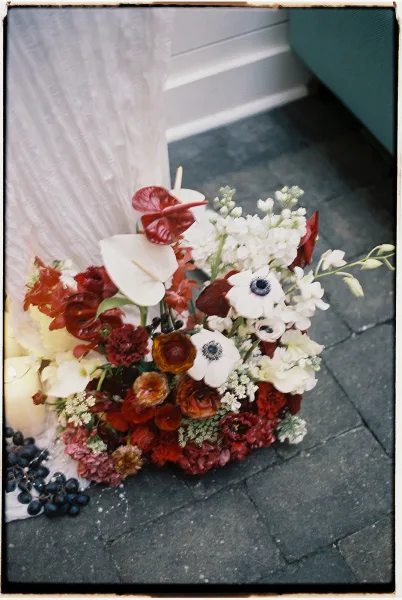 Bridal bouquet with anemone wedding bouquet blooms, calla lilies and deep red flowers wrapped in a veil on stone pavement by a doorway