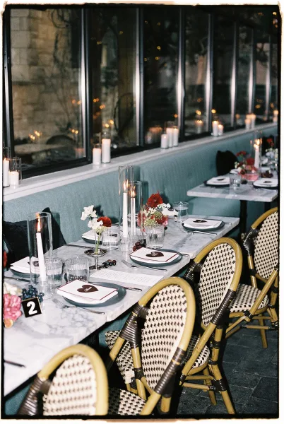 Reception tablescape with candlelit wedding reception glow, white taper candles in glass hurricanes on a marble table by window wall and banquette seating