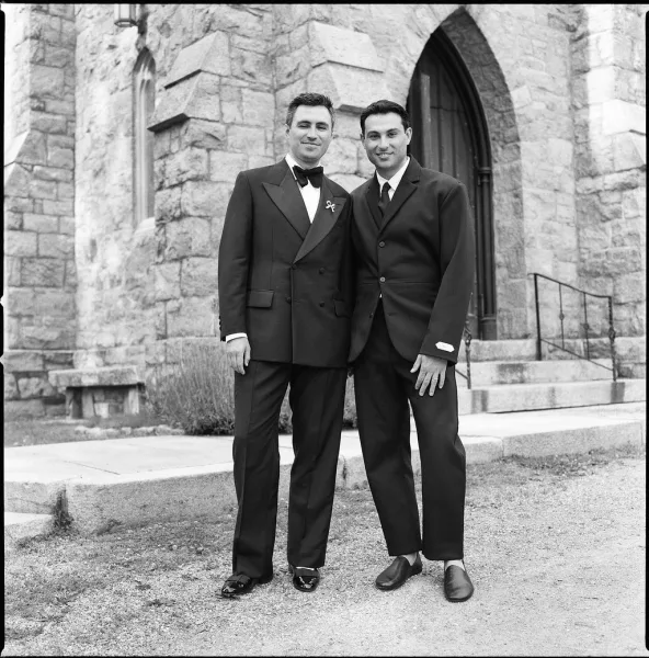 Groom and groomsman portrait on stone church steps, a best man portrait framed by an arched doorway, with classic bow tie detail.