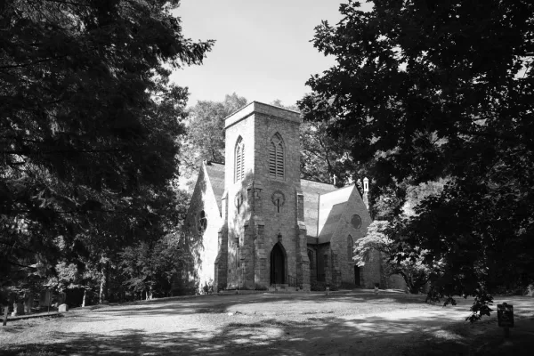 Church exterior showcasing stone chapel architecture with an arched doorway, framed by trees and sky.