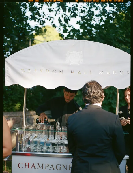 Champagne cart with champagne bottles and flutes under a canopy awning, custom signage displayed in a lush outdoor garden setting