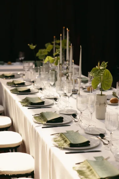 Reception tablescape for long banquet table decor, taper candles lining the center and softly glowing against a dark backdrop.