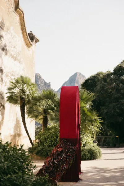Ceremony backdrop with a velvet wedding arch amid bold red ceremony decor, framed by palm trees against a stucco wall and distant mountains.