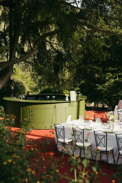 Wedding bar setup for an outdoor wedding bar, styled with fresh greenery on a red terrace floor in a garden setting.