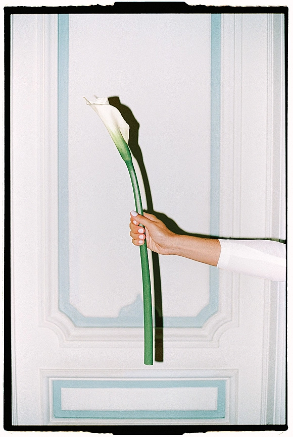 Calla lily bouquet held by a manicured hand, a single stem bridal bouquet with long green stem against a white paneled wall shadow