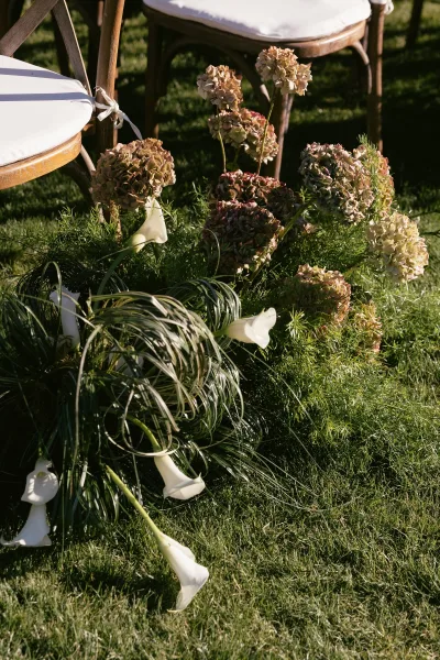 Ceremony aisle flowers with calla lily aisle decor line the walkway on a grass lawn, creating a simple, romantic path.