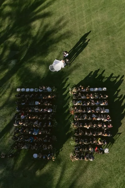 Ceremony moment at an outdoor wedding ceremony as the bride with a flowing veil faces her groom on a grass lawn with long shadows.
