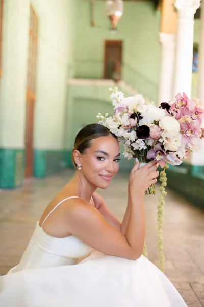 Bridal portrait of a bride with bouquet, featuring orchid blooms, framed by green walls and columns in an indoor setting.