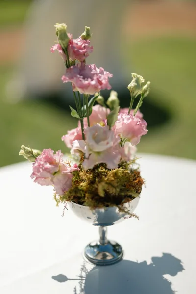 Wedding centerpiece as a compote flower arrangement with pink lisianthus, set on a white tablecloth on a grass lawn.