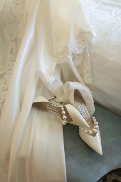 Bridal shoes, pearl strap heels resting on a bridal gown, captured as an elegant, timeless wedding detail.