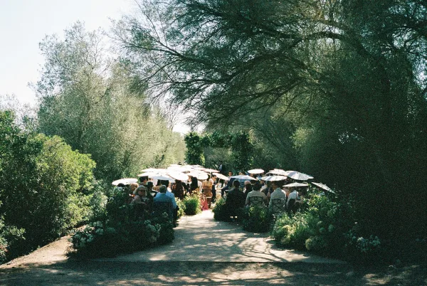Outdoor ceremony setup featuring garden ceremony decor and a greenery arch beneath trees along a dirt path.