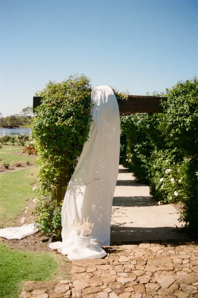 Wedding signage with a fabric welcome sign hanging from a wooden arbor in a tranquil lakeside garden at the ceremony entrance.