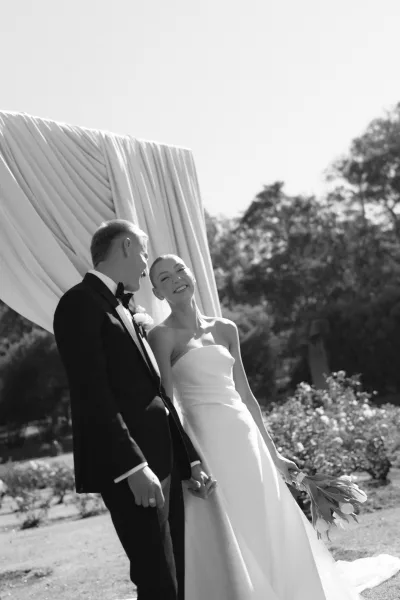 Couple portrait with the bride and groom holding hands, her white tulip bouquet nestled between them as they share warm smiles and quiet joy.