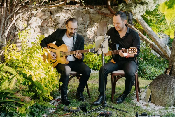 Wedding musicians, a wedding guitar duo of live acoustic guitarists performing by a stone wall amid garden greenery with a microphone stand