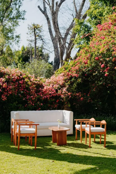 Wedding lounge setup for outdoor lounge seating with a coffee table on a grass lawn framed by flowering bushes and trees