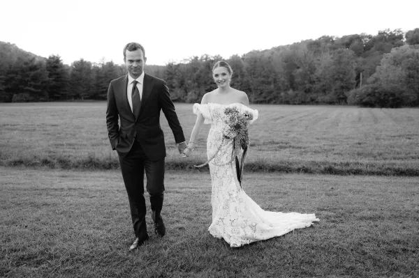 Couple portrait in a black and white wedding portrait style, bride and groom holding hands, bride with bouquet in a grassy field with hills