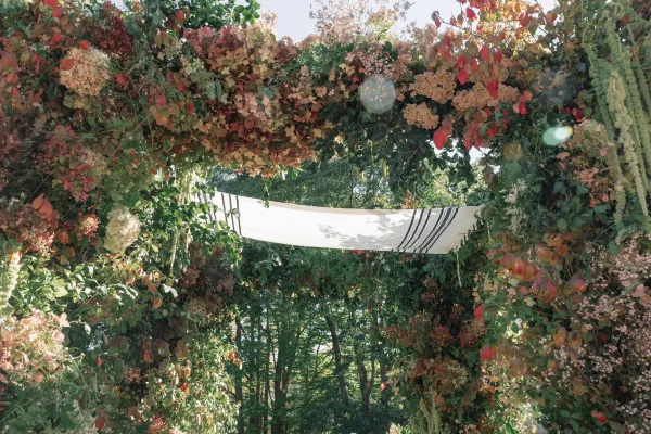 Wedding ceremony arch with floral arch wedding design, draped fabric and hydrangeas, framed by garden trees under open sky