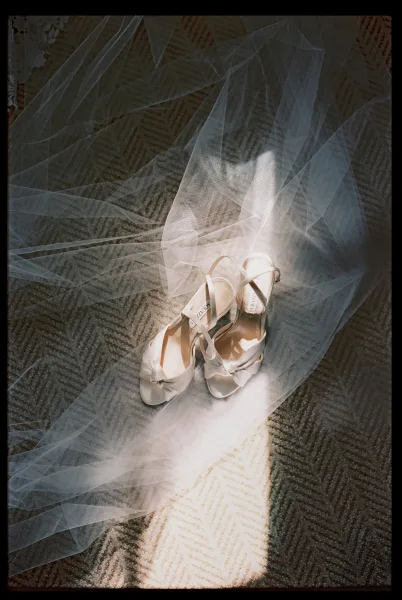 Bridal shoes in a wedding shoes flat lay with white strappy heels and bow detail under sunlight on patterned carpet shadows