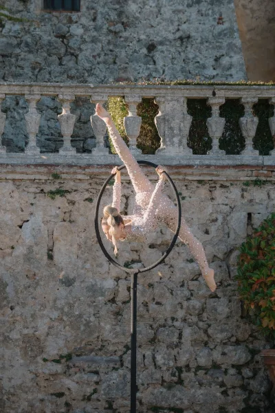 Aerialist wedding entertainment with an aerial hoop act, a performer in a pearl-studded bodysuit poses against a stone balustrade and greenery.