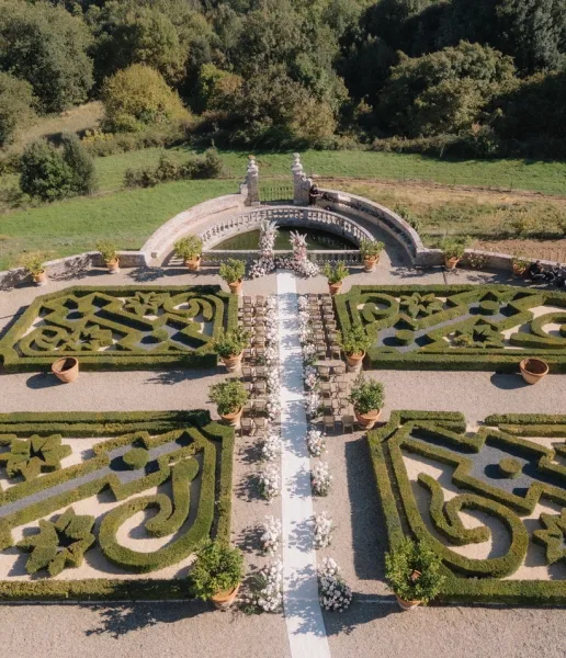 Garden ceremony setup featuring refined outdoor ceremony decor and a white aisle runner, framed by formal hedges and a stone balustrade.