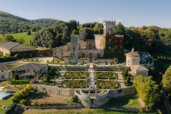 Castle wedding venue with an outdoor ceremony setup, framed by a stone balustrade, overlooking rolling hills and lawns beneath a blue sky