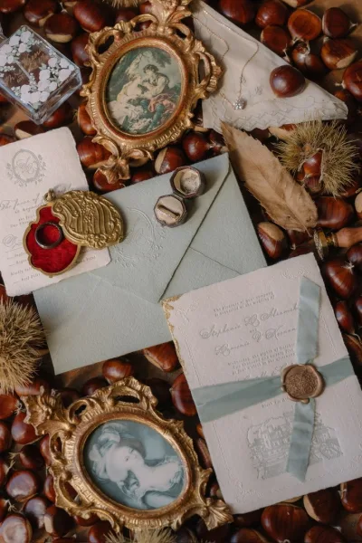 Wedding invitation suite featuring vintage wedding invitations sealed with a wax seal, arranged among chestnuts, chestnut shells, and a dried leaf.