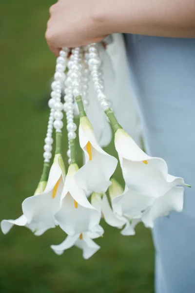 Calla lily bouquet as a white wedding bouquet, sleek long stems wrapped with pearls for a minimalist, modern bridal look.