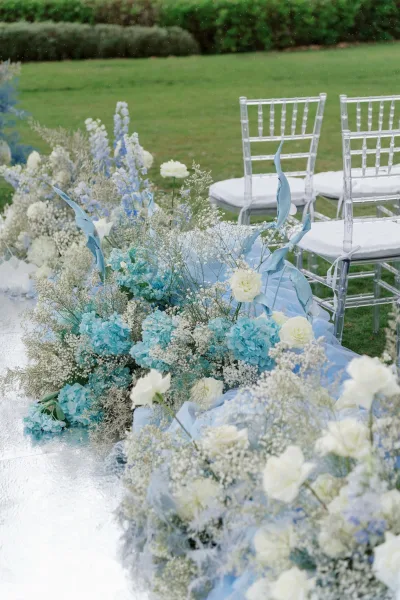 Ceremony aisle decor for an outdoor ceremony setup featuring a mirrored aisle runner flanked by lush florals on a grass lawn.