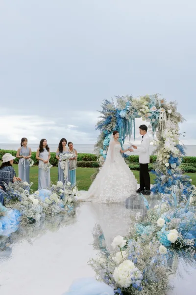 Wedding vows at an outdoor wedding ceremony under a floral arch, the couple framed by an ocean view.