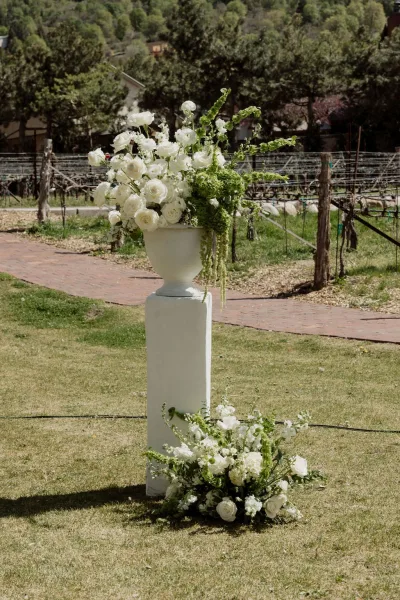 Ceremony flowers create an altar flower arrangement with white florals, set on a grass lawn against vineyard rows on a hillside.